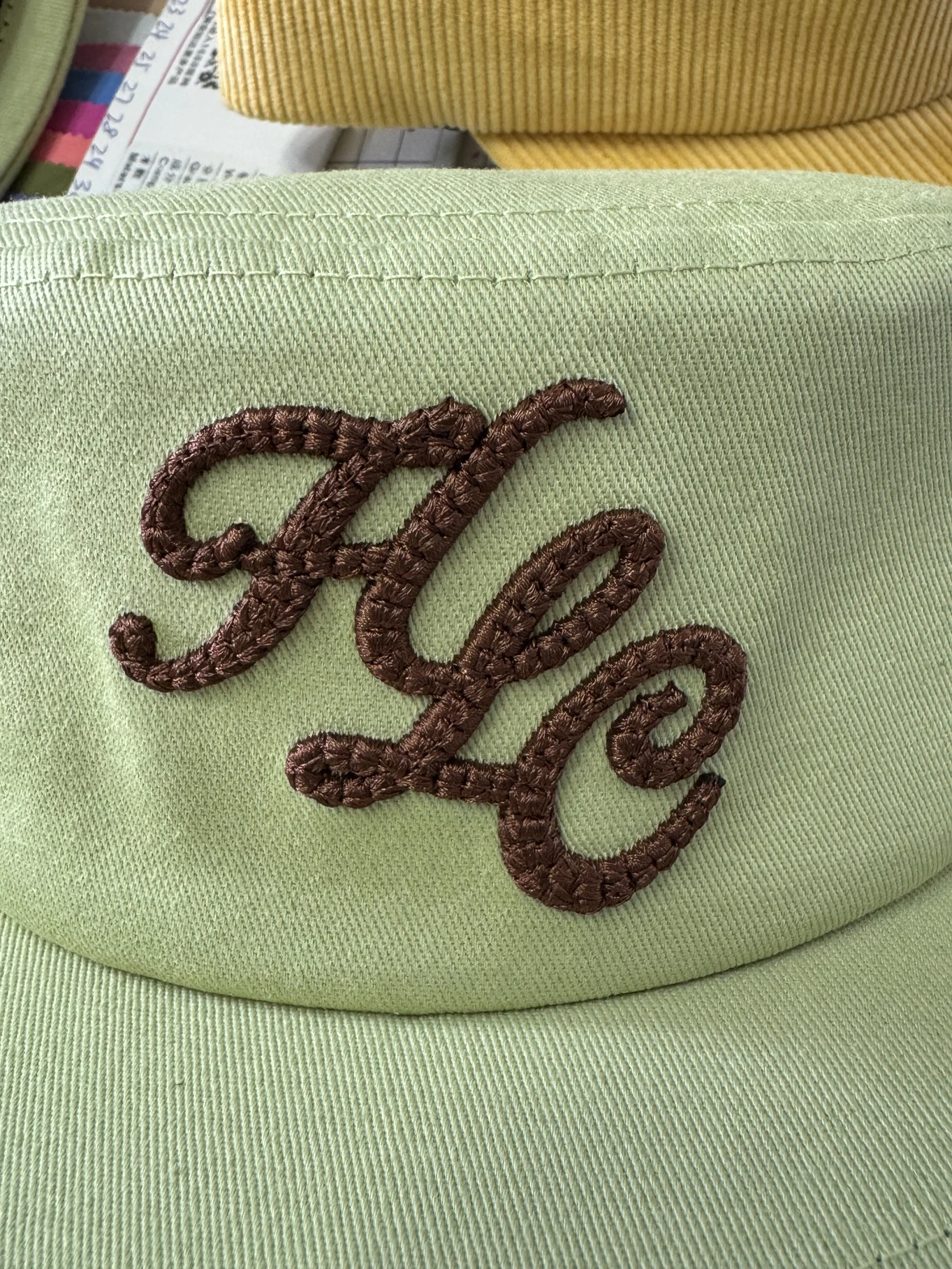 Raised brown script embroidery on sage-green twill fabric.