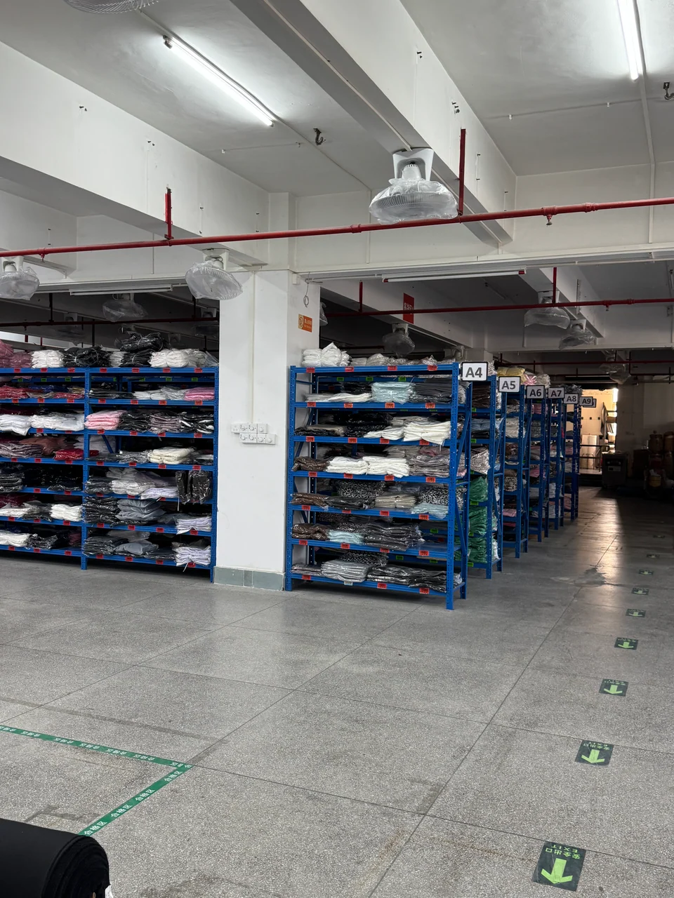 Packed garments arranged on labeled blue shelving in a stock storage area.
