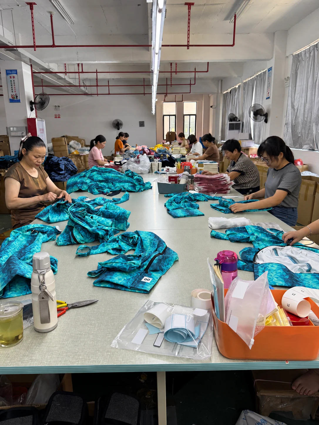 Workers finishing and packing garments; client identifiers anonymized.