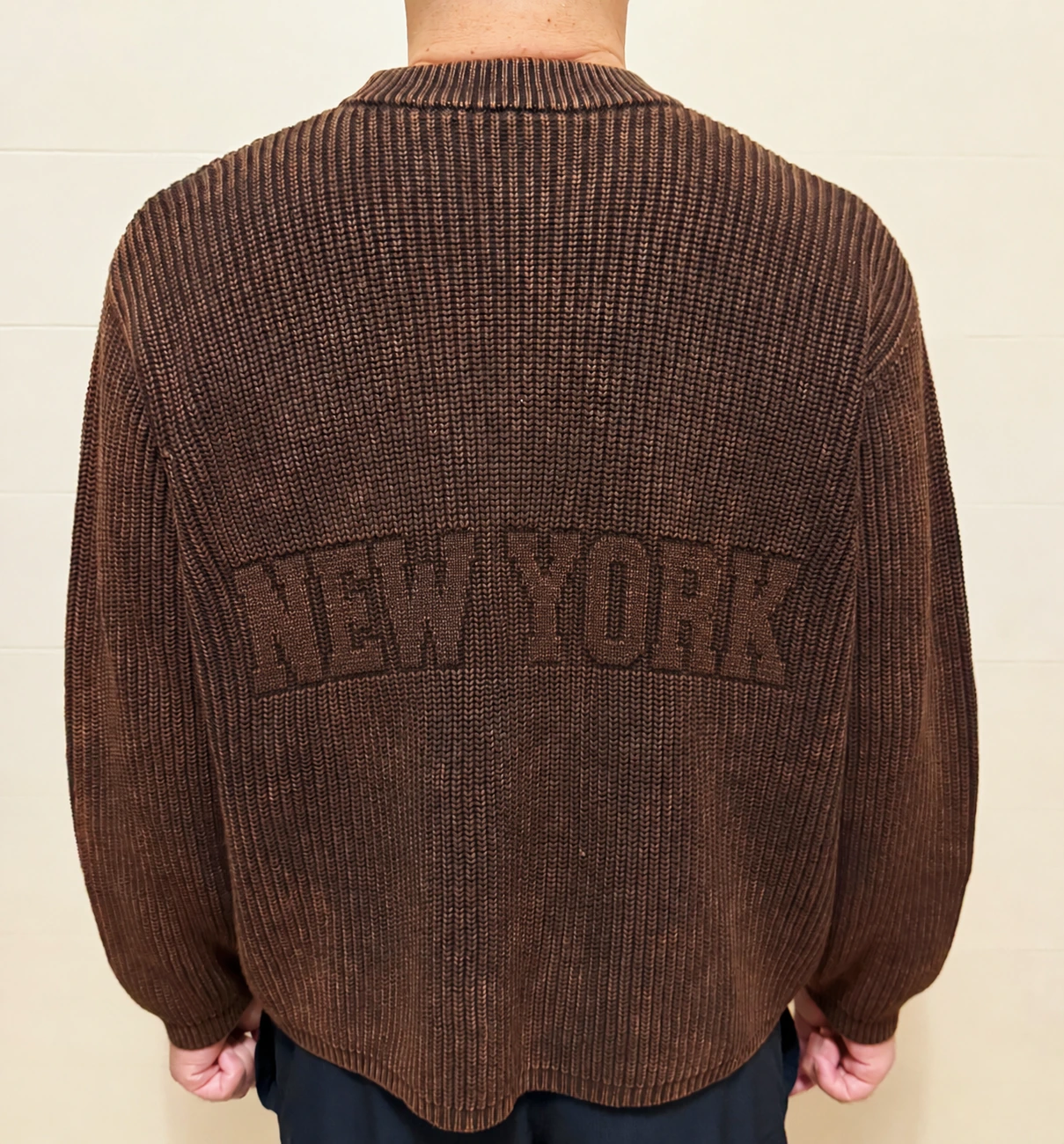 Developed brown sweater sample, back view with anonymized tonal knit relief lettering.