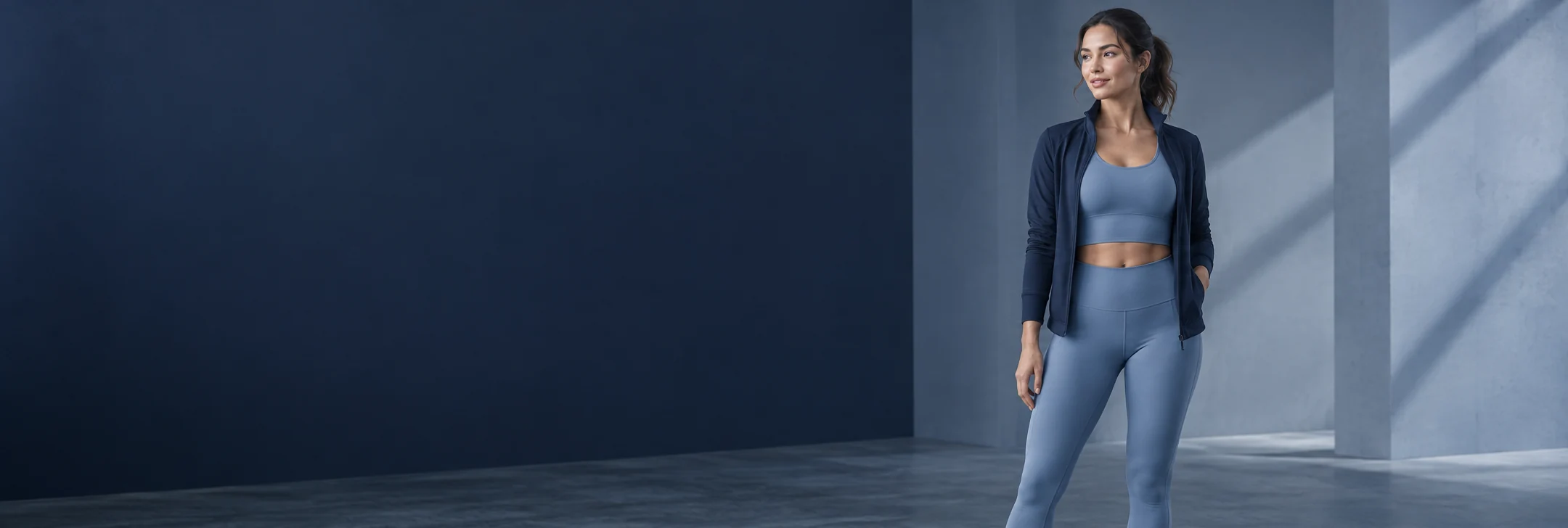 Athlete wearing a mist-blue sports top and leggings with a navy training jacket.